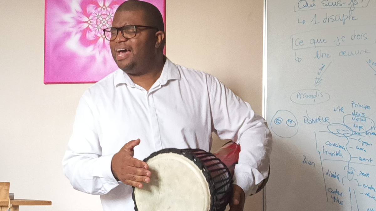 Romaric chantant et accompagnant au djembé devant le tableau d'enseignement des vertus